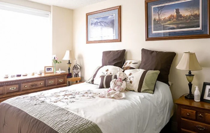 A cozy bedroom with a neatly made bed and decorative pillows, featuring framed artwork and a plush toy.