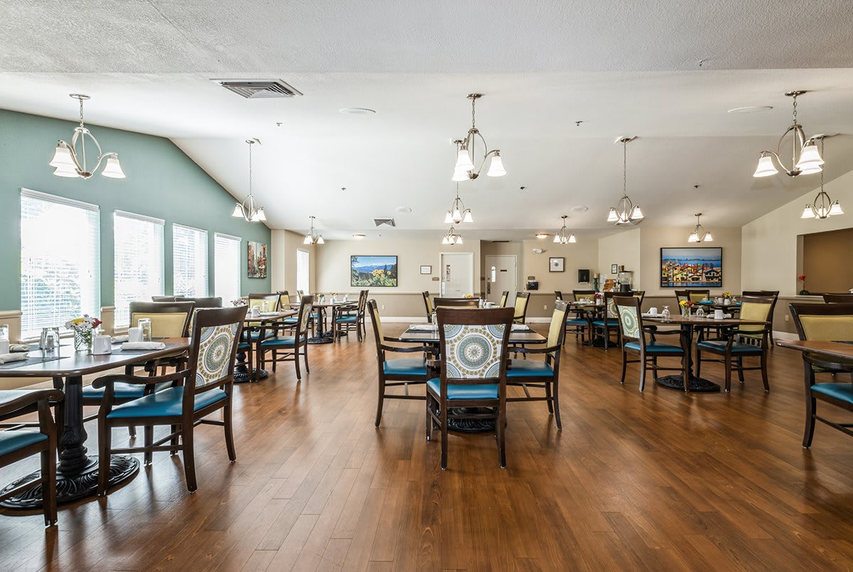 A spacious and well-lit dining room with tables and chairs arranged neatly on a wooden floor.