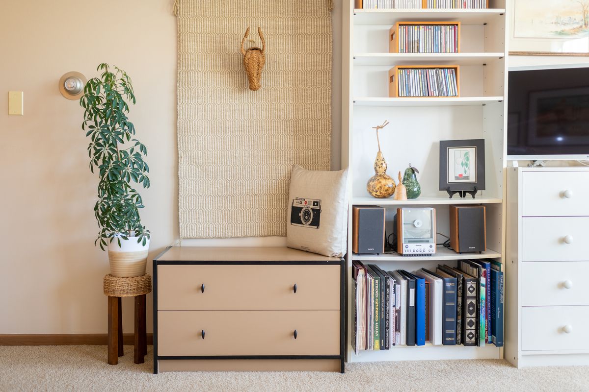 A cozy interior space featuring a bookshelf, drawer storage, and decorative elements including a plant and various books.
