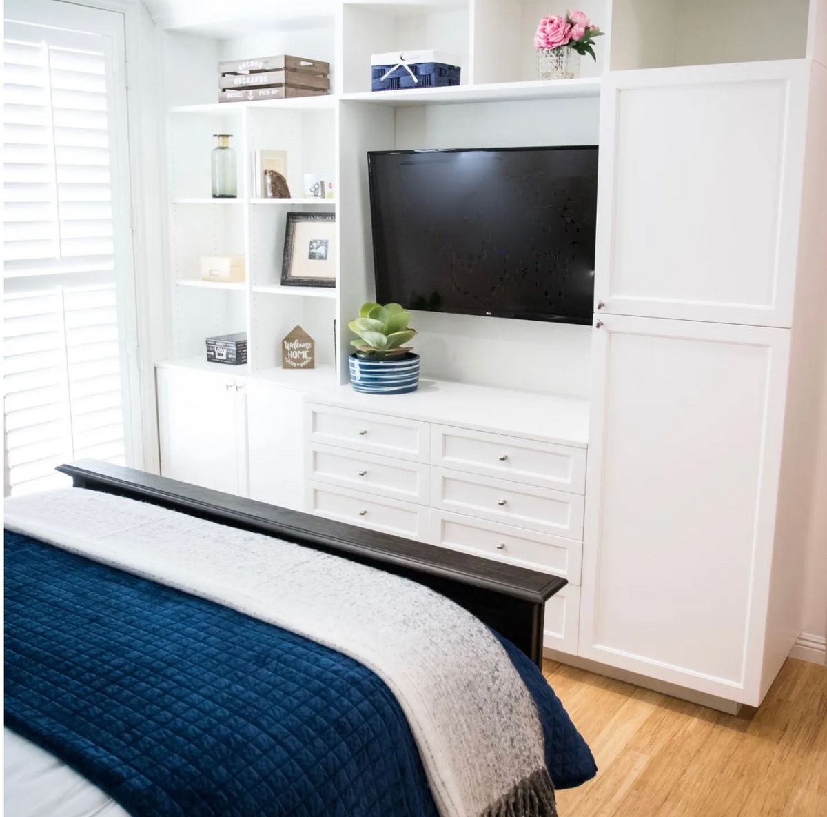 A cozy bedroom with white built-in furniture and a television.