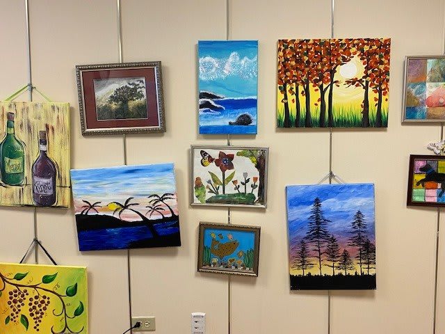 A collection of colorful paintings displayed on a gallery wall, featuring various landscapes and nature scenes.