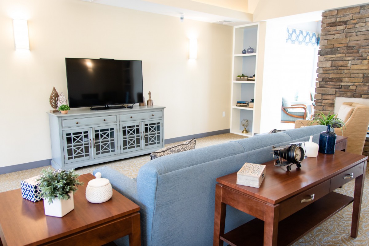 A cozy living room featuring a television on a stylish cabinet, a comfortable blue couch, wooden side tables, and built-in shelves.