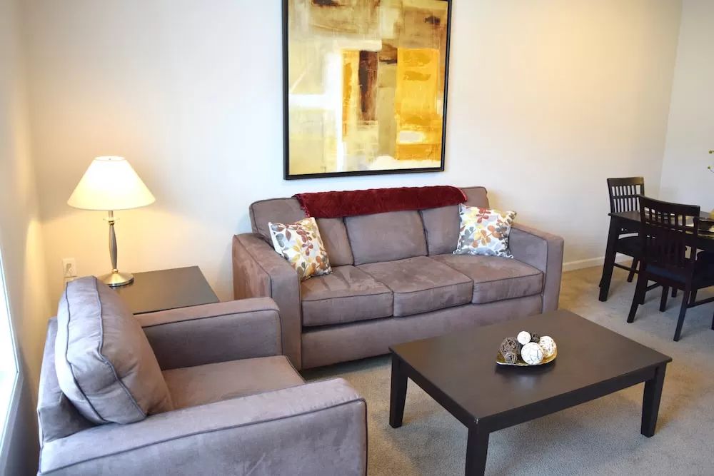 A cozy living room with a sofa, armchair, and coffee table, complemented by a lamp and wall artwork.