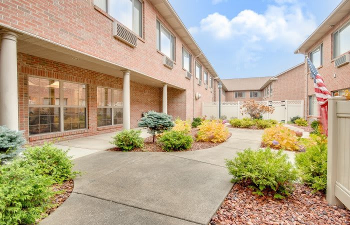 A brick building with a landscaped courtyard featuring various shrubs and paved walkways.