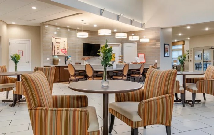 A modern lobby seating area featuring striped chairs, round tables, and elegant lighting.