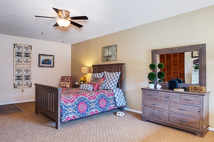 A cozy bedroom featuring a wooden bed with colorful bedding, a matching dresser, and decorative artwork on the walls.