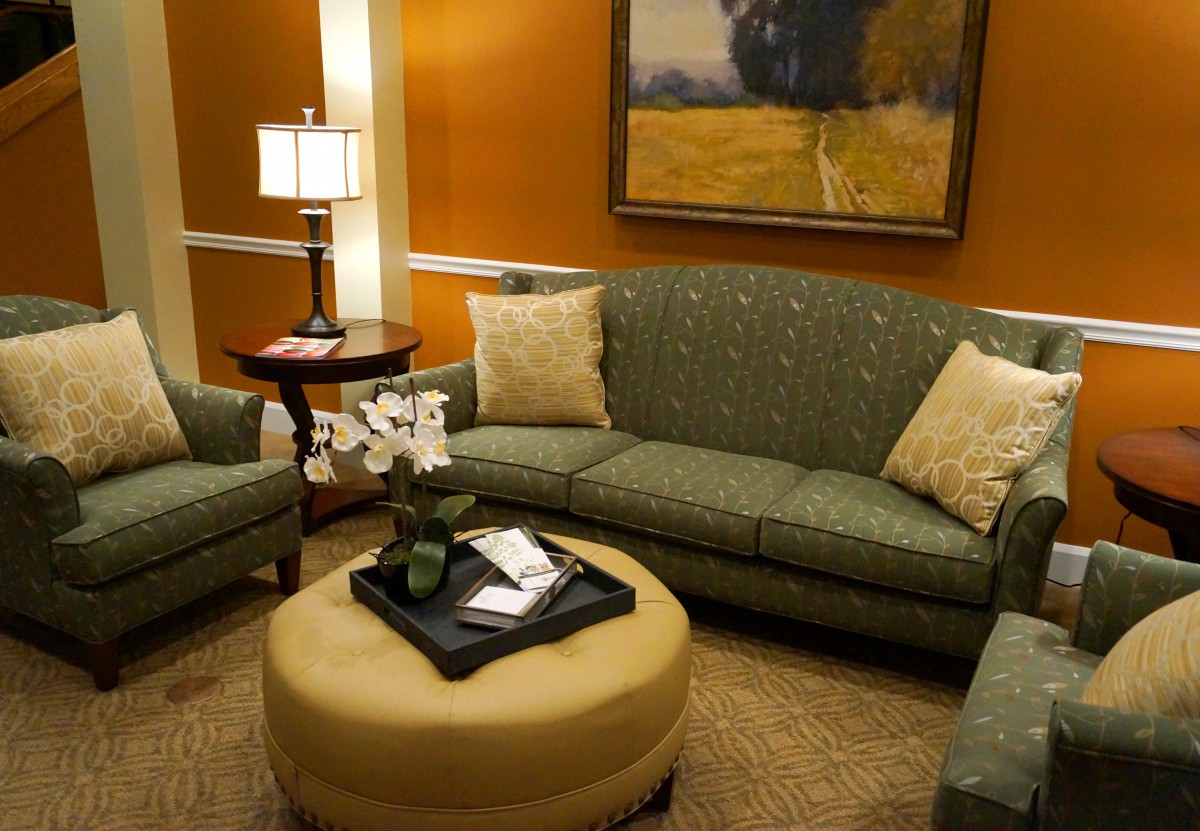 A cozy living room with a green sofa set, round ottoman, and decorative elements.