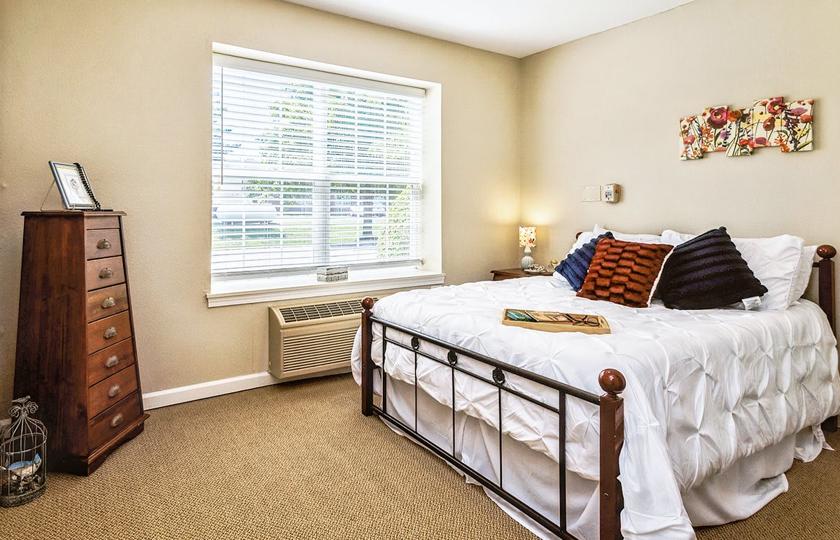 A cozy bedroom with a white bed, natural light streaming through the window, and minimal decor.