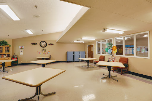 A spacious community room featuring tables and chairs, complemented by natural lighting from large windows.