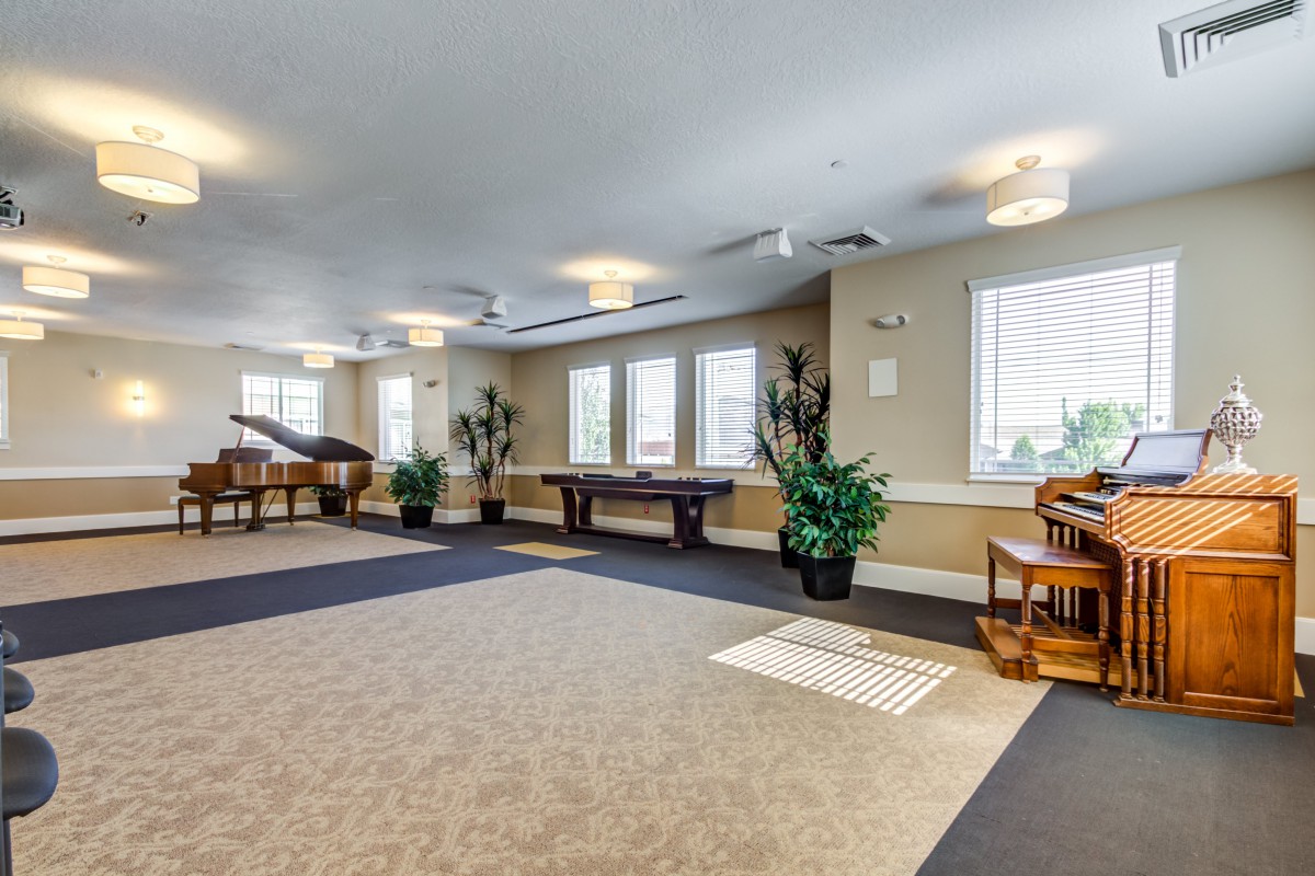 A spacious game room featuring a pool table and piano, with ample natural light from large windows and decorated with potted plants.