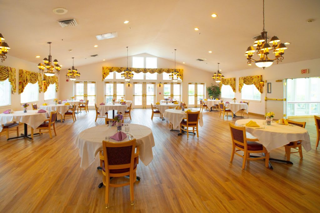 A spacious and well-lit dining room with wooden floors, neatly arranged tables, and comfortable chairs.