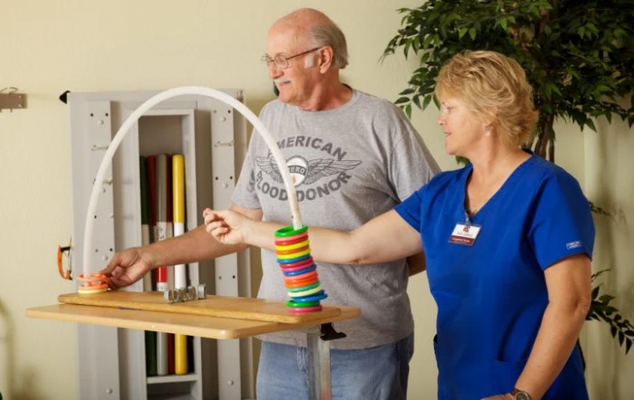 An elderly man is guided by a therapist during a rehabilitation exercise session.