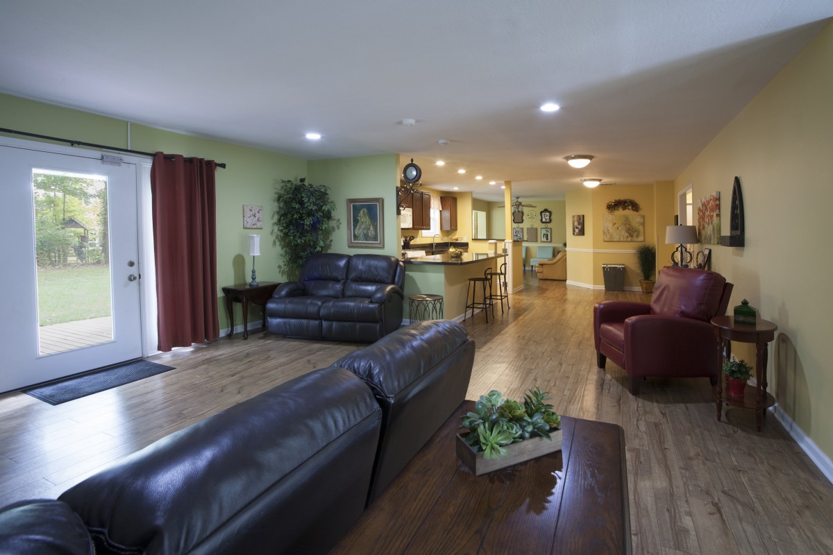 A spacious open-plan living area with a view of the kitchen, featuring leather sofas and warm wooden flooring.
