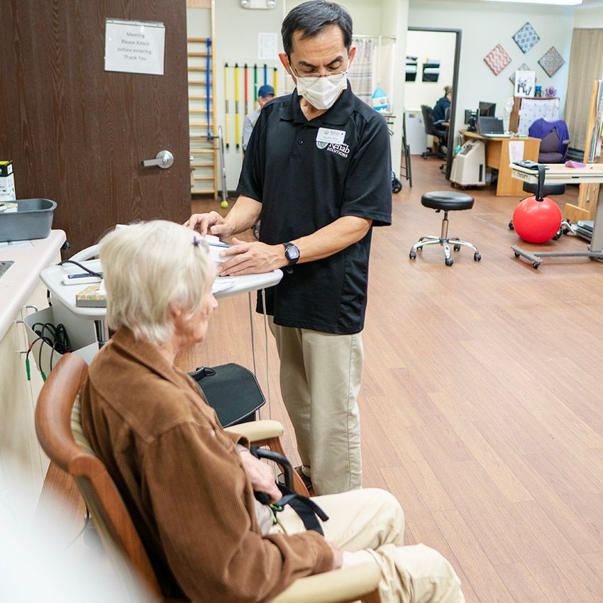 A healthcare professional consults with an elderly patient in a medical office setting.