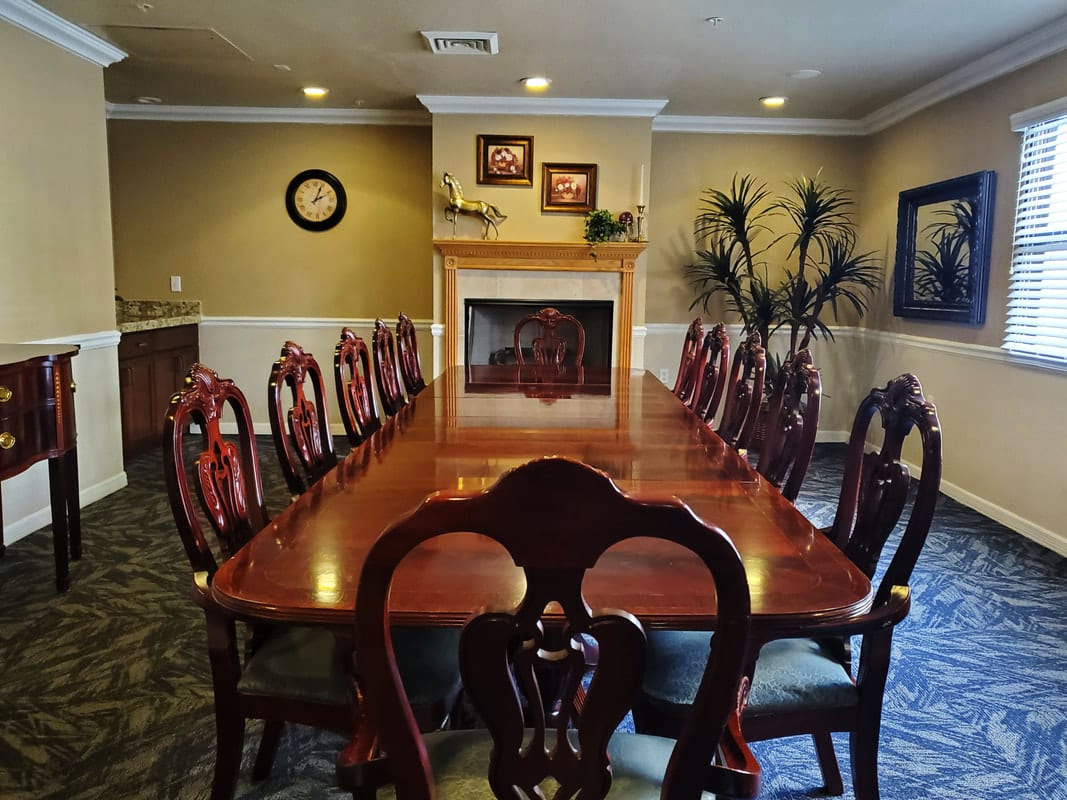 A classic dining room featuring a long wooden table surrounded by elegant chairs, with a fireplace and decorative elements in the background.
