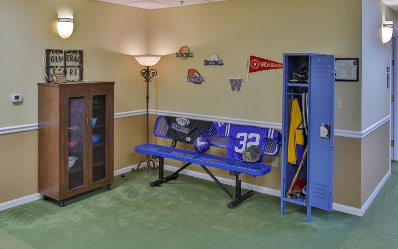A sports-themed room featuring a blue bench, sports helmets, and a locker with decorative pennants on the wall.