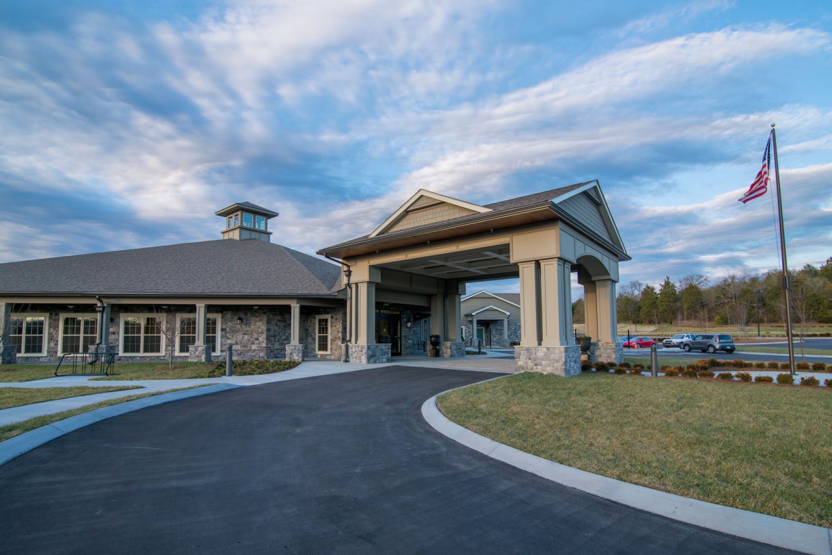 An elegant building entrance with a covered driveway against a scenic sky backdrop.