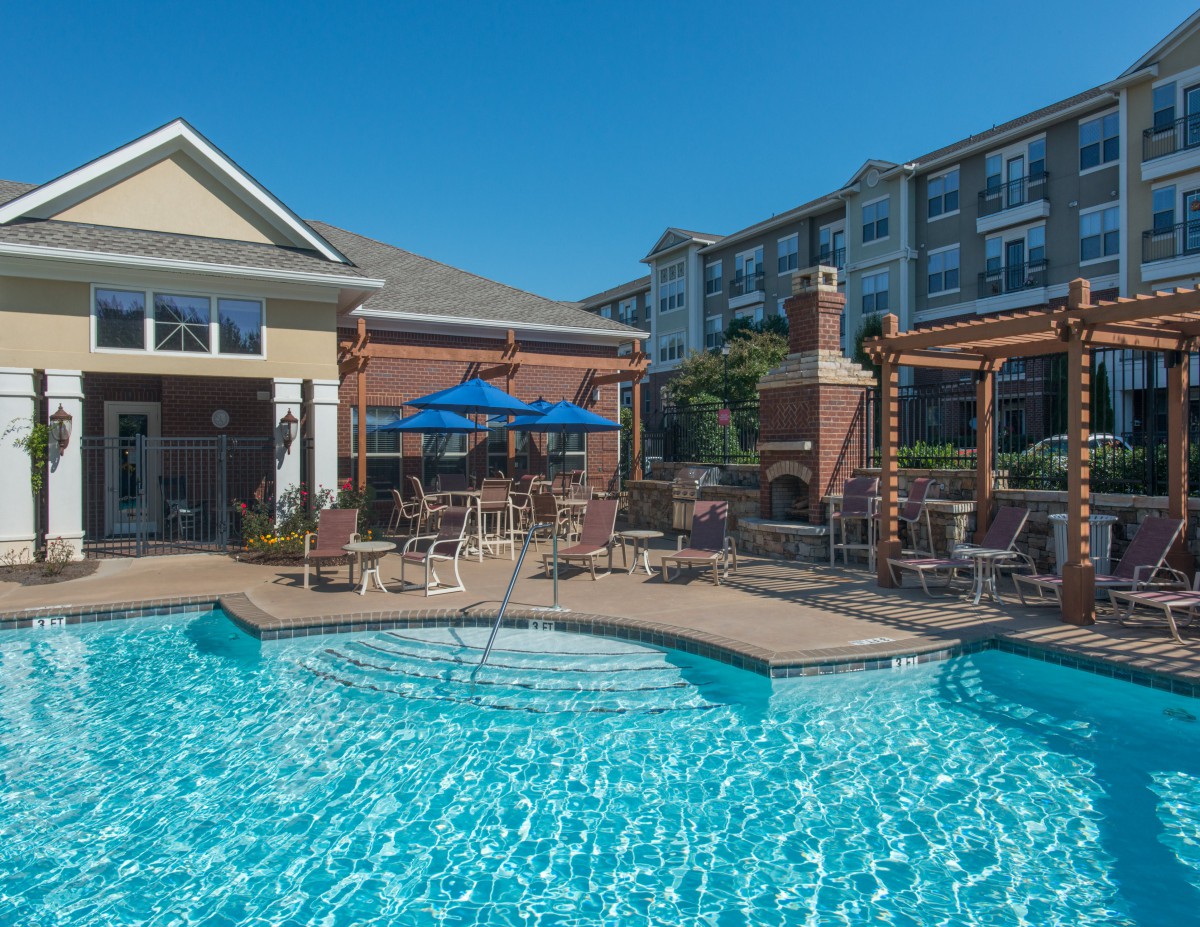 A sunny day at a residential apartment complex featuring an outdoor swimming pool and patio area.
