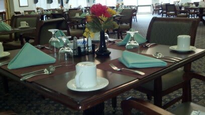 A neatly set dining table in a restaurant with a flower arrangement, glasses, napkins, and a cup.