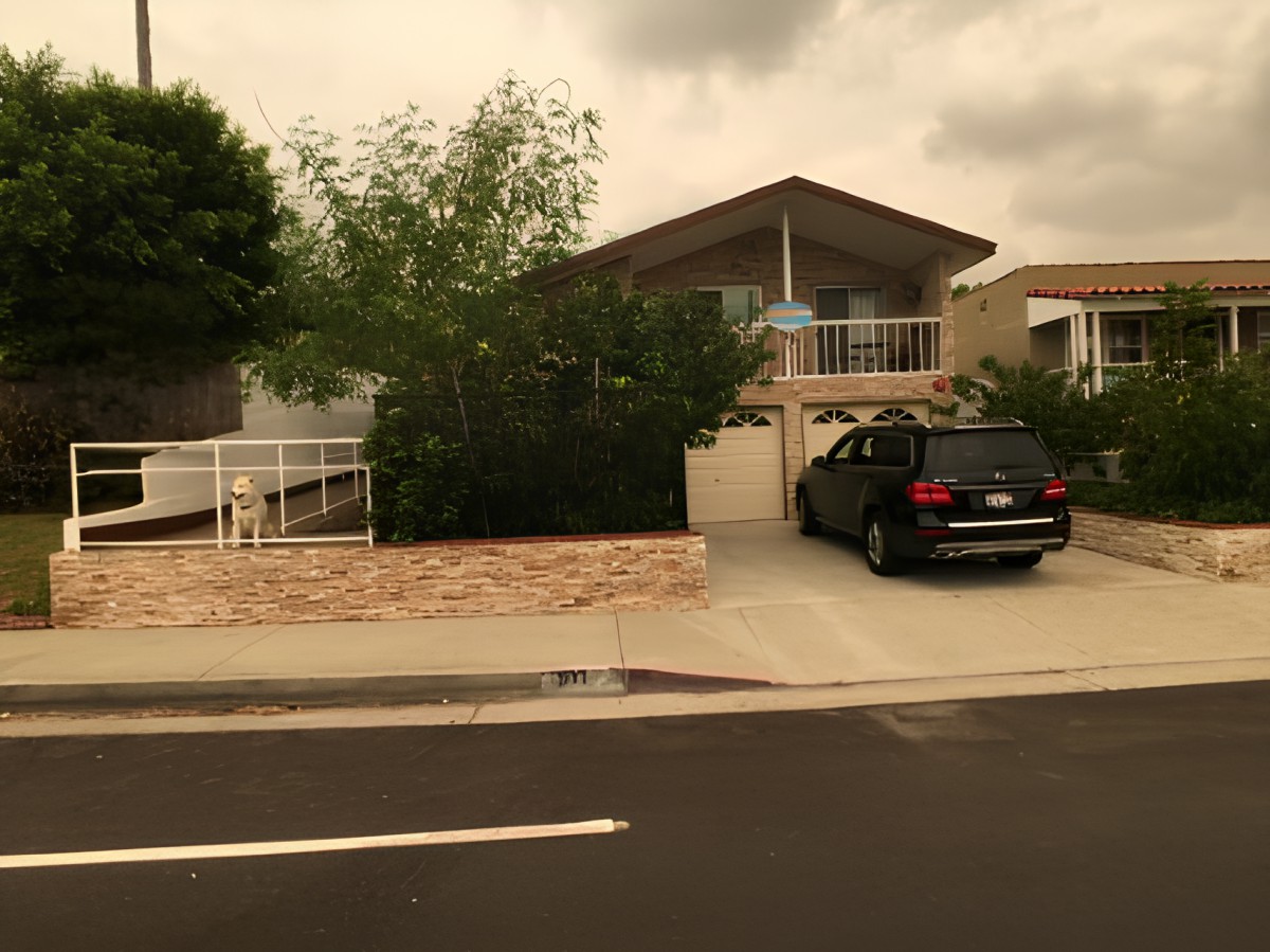 A suburban house with a driveway, garage, and parked car on a cloudy day.