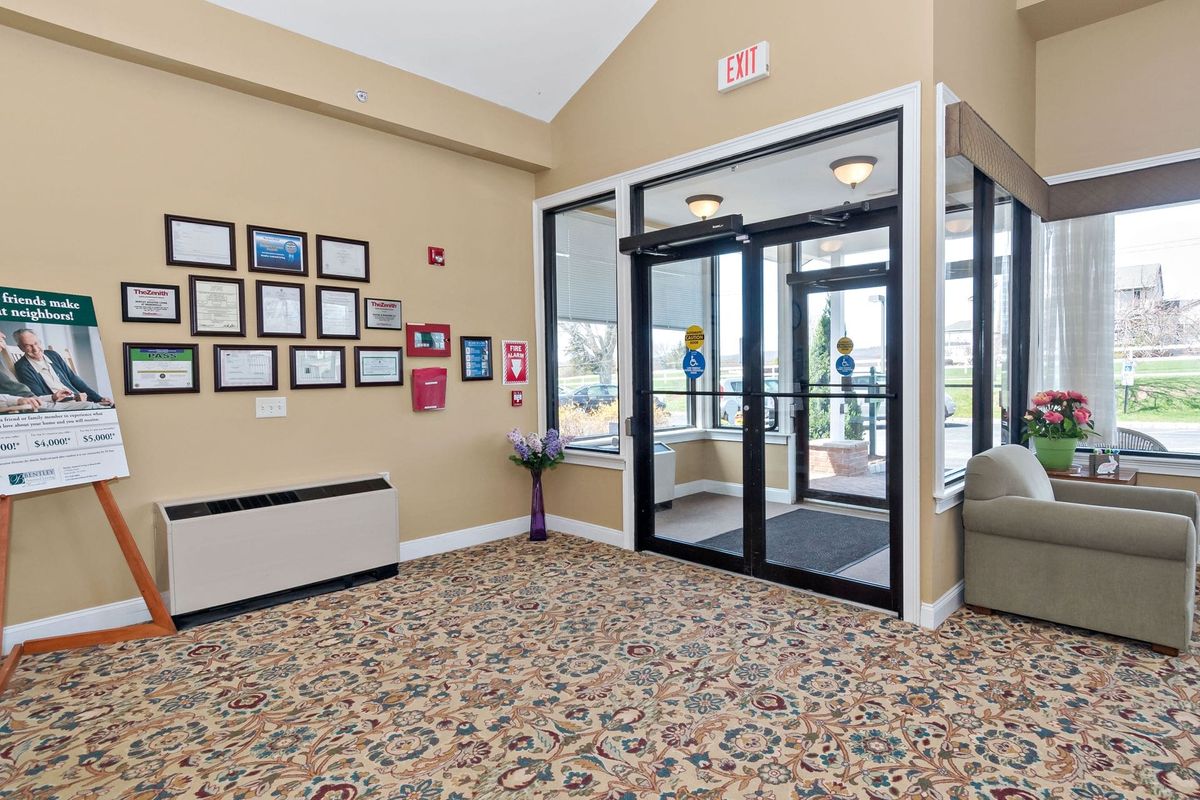 A hotel lobby with glass entrance doors, decorated walls, and a patterned carpet.