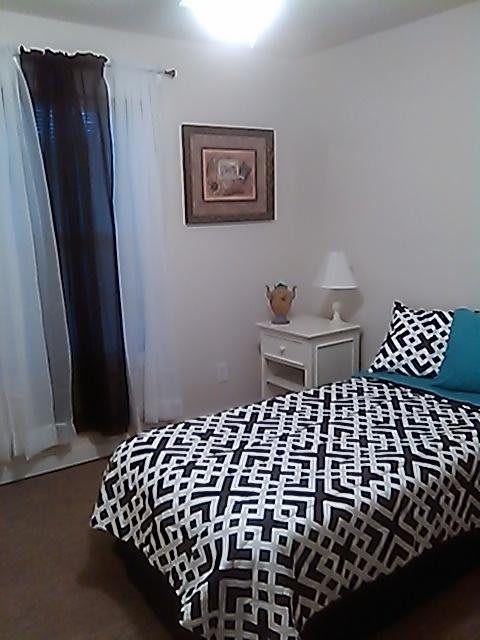 A cozy bedroom featuring a single bed with black and white patterned bedding, complemented by a teal pillow, a nightstand with a lamp, and wall art.