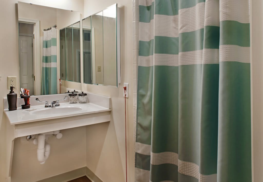 A bathroom with a large mirror, a sink, and a green striped shower curtain.