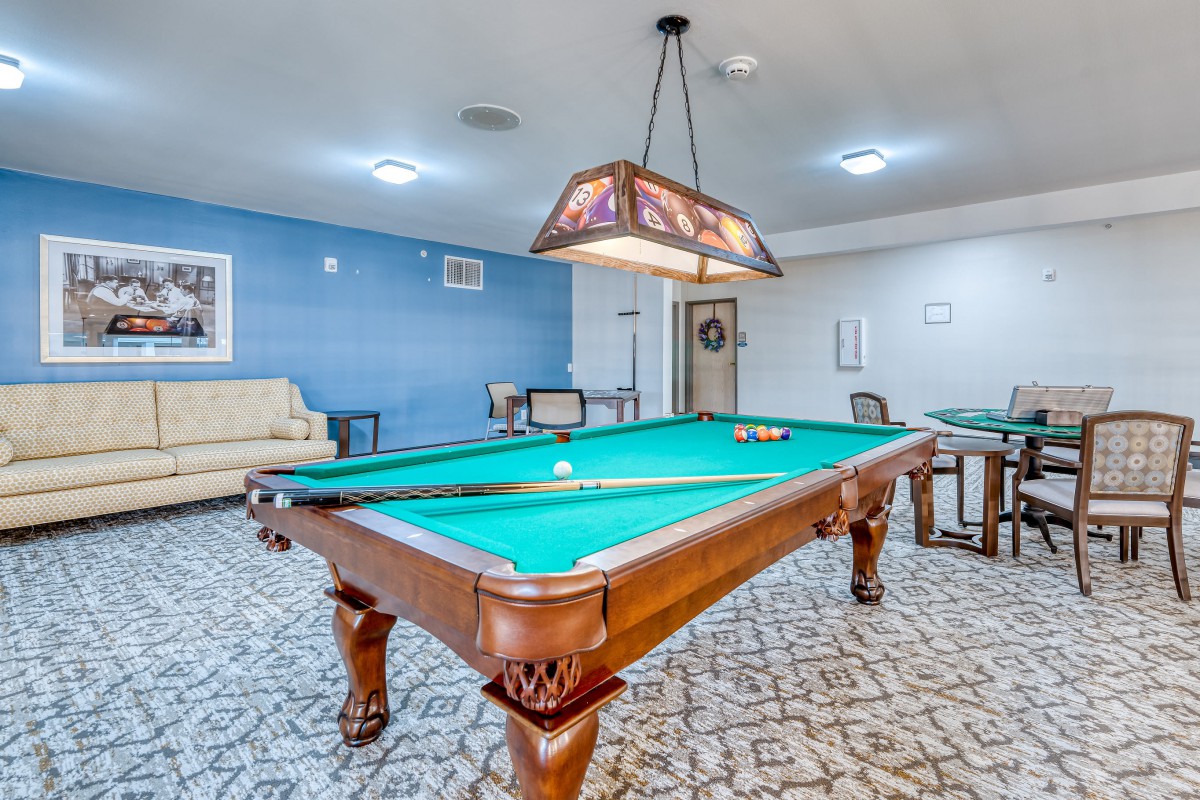 A spacious game room featuring a pool table under stylish lighting, with comfortable seating in the background.