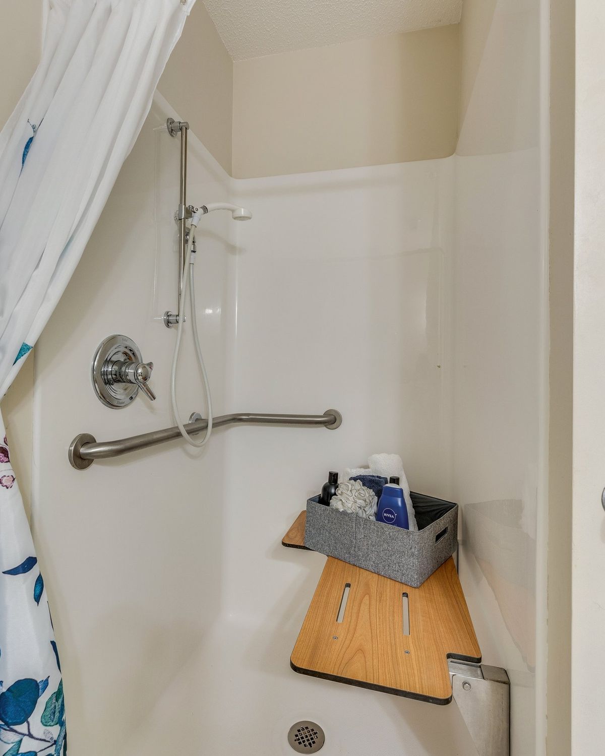 A bathroom shower equipped with safety features, including a grab bar and a bath seat.