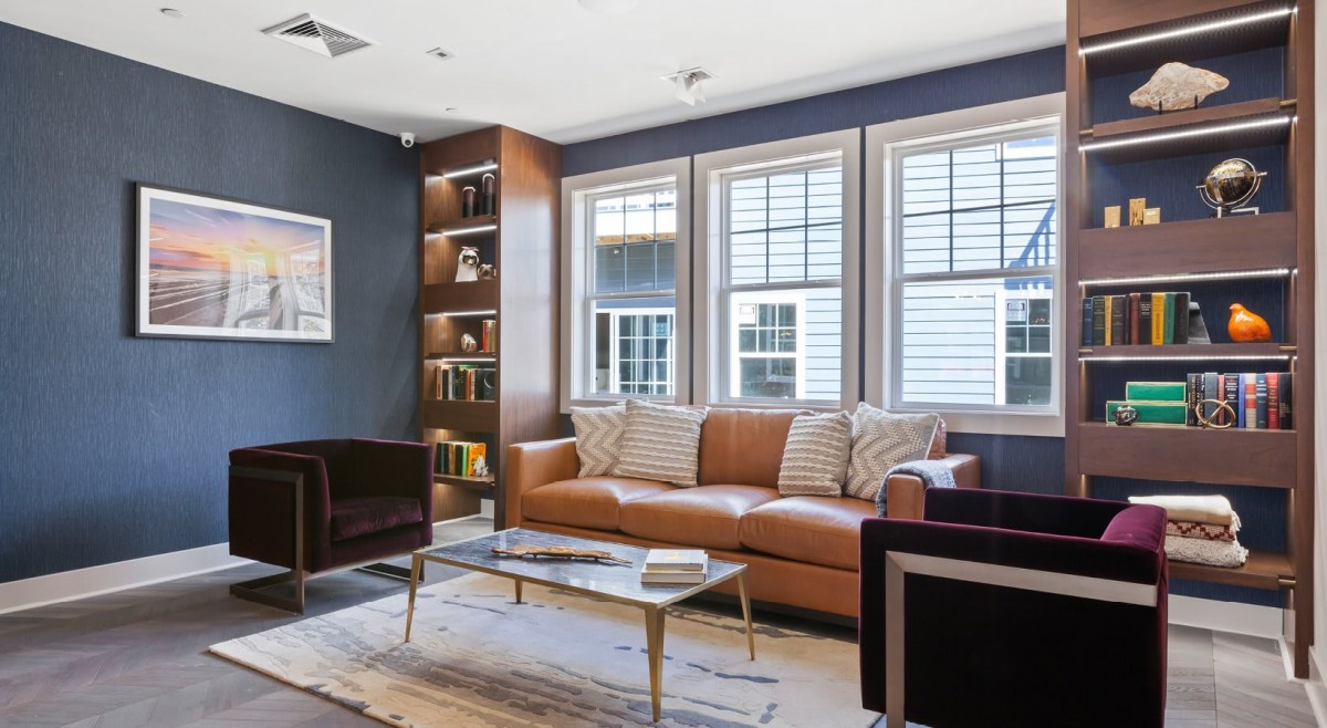 A modern living room with a leather sofa, coffee table, and built-in bookshelf by the windows.