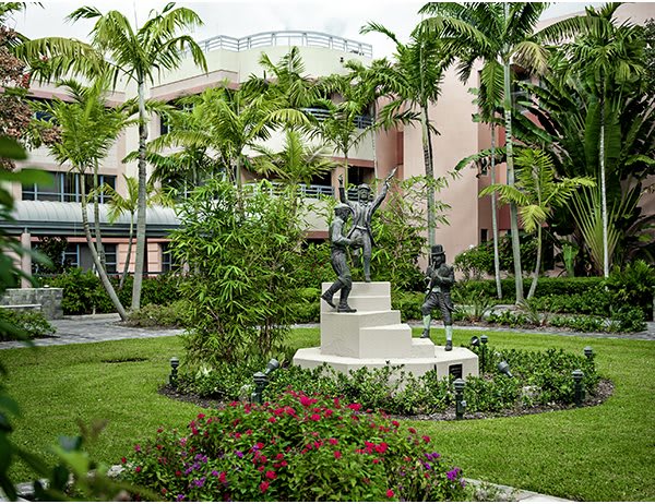 A beautifully landscaped garden featuring statues surrounded by lush greenery and palm trees.
