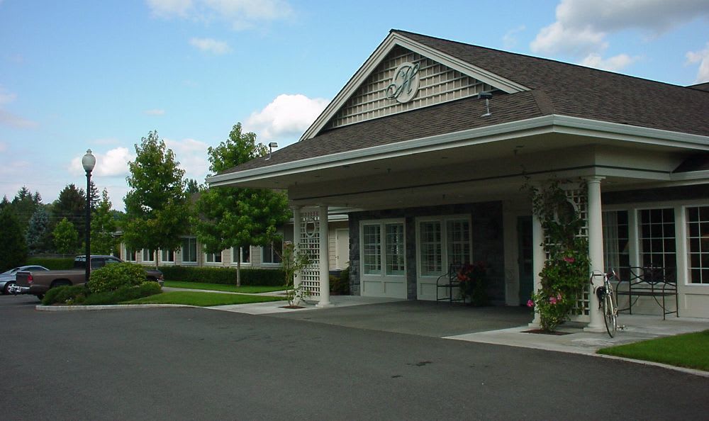 An exterior view of a building entrance with a covered driveway and surrounding greenery.