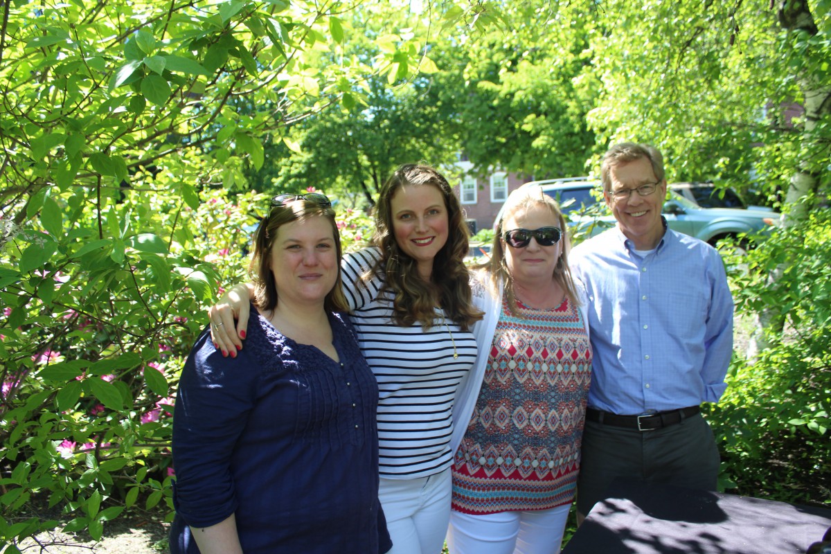 A group of four people standing together outdoors on a sunny day.