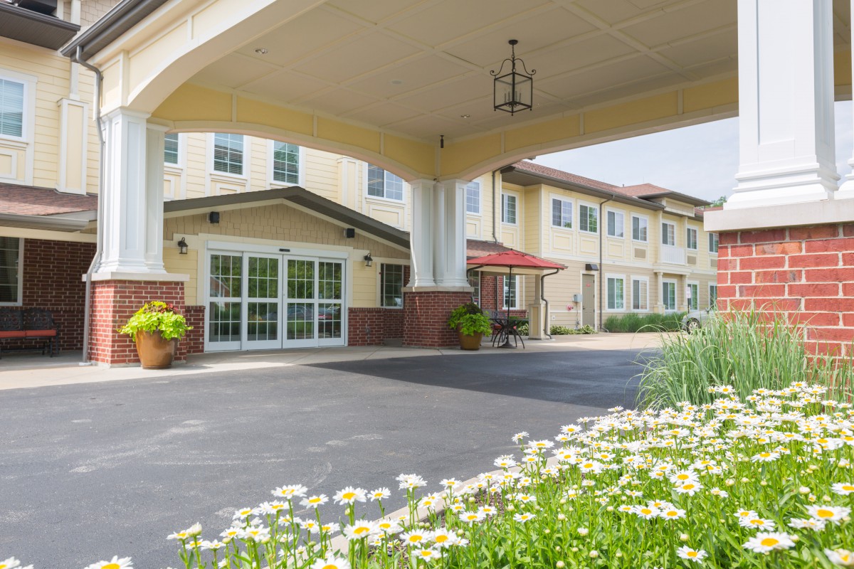 Entrance to a two-story building with a covered driveway and landscaped surroundings.