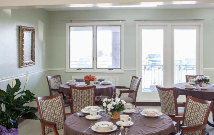 A well-lit dining room with several round tables set for a meal, featuring elegant tableware and floral centerpieces.