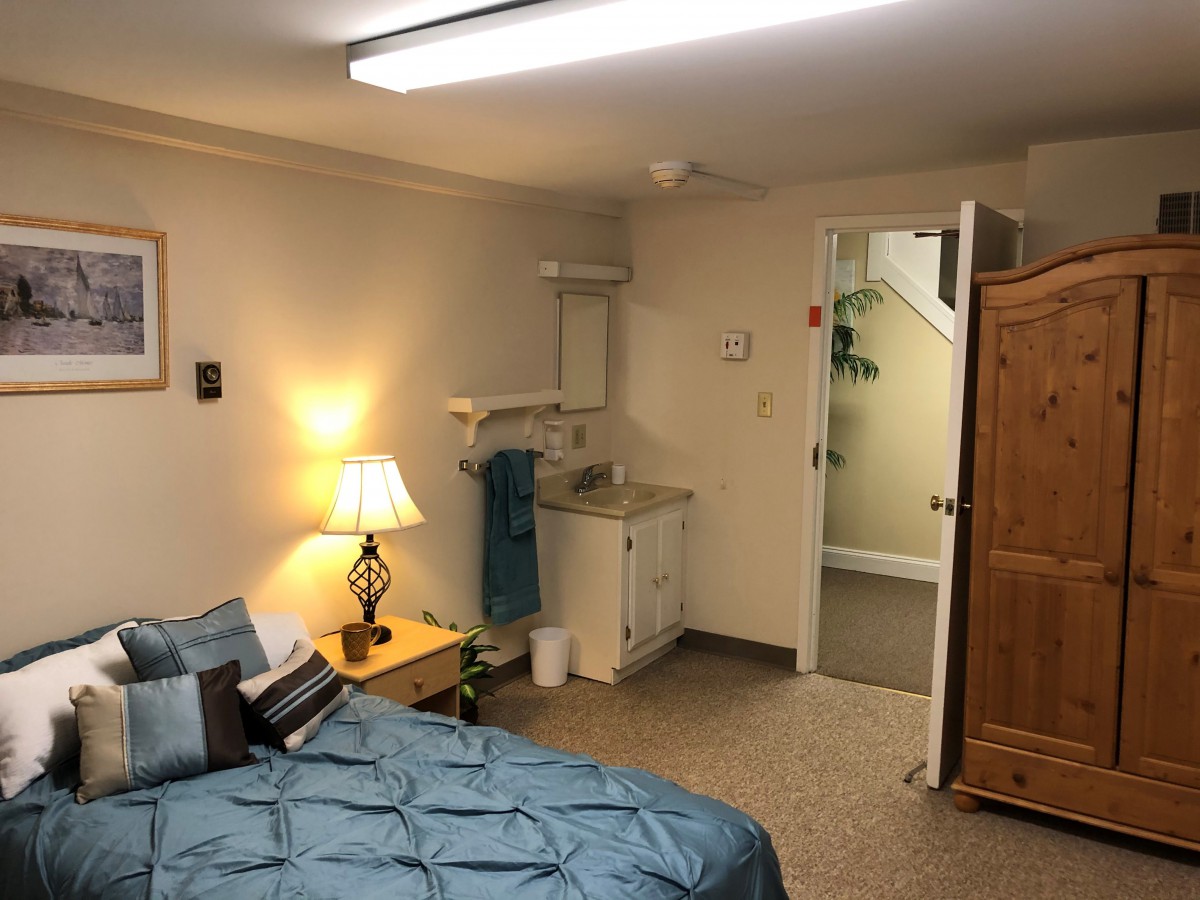 A cozy bedroom with a bed, lamp, sink, and wardrobe.