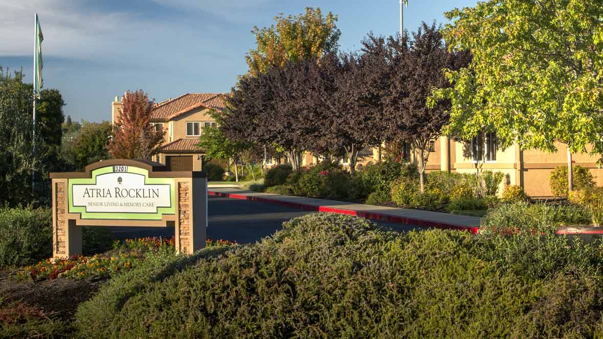 Entrance of an apartment complex with lush landscaping and clear signage.