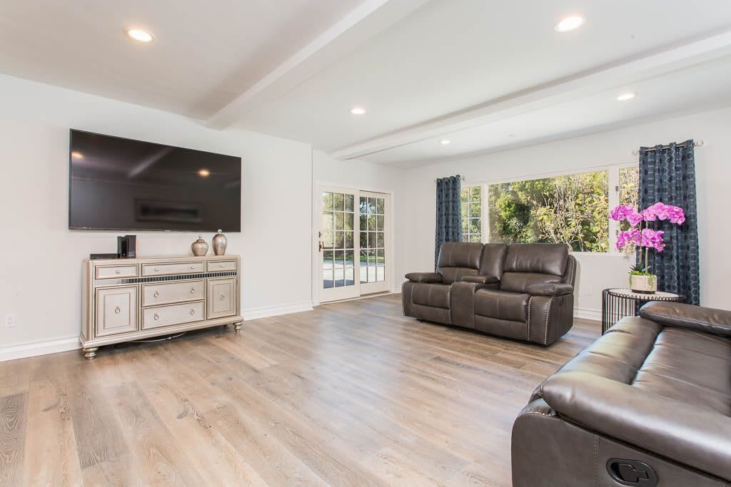 A modern and spacious living room featuring comfortable leather seating, a large television, and wood flooring.