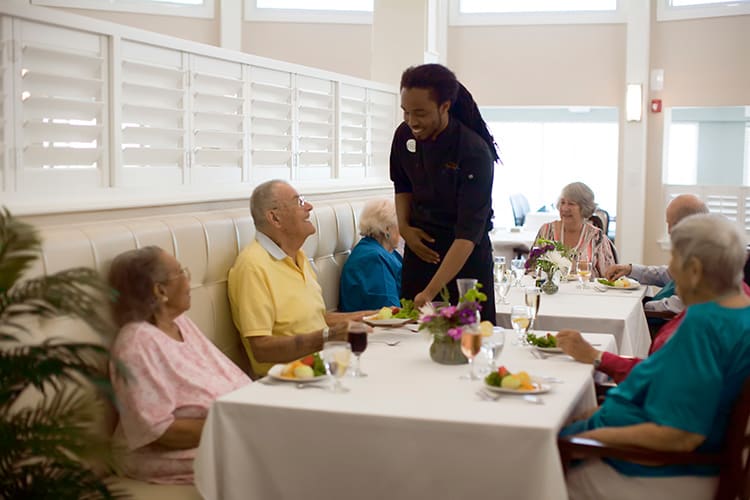 A server interacting with elderly individuals at a dining table in a restaurant setting.