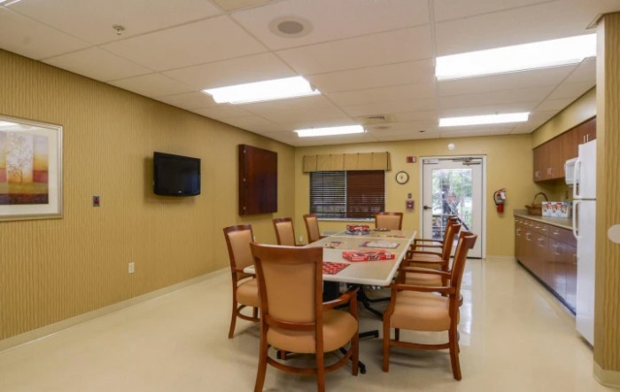 A well-lit conference room featuring a large meeting table surrounded by chairs, with a television mounted on the wall.