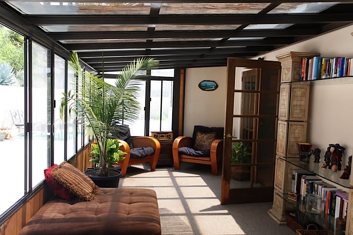 A cozy sunroom filled with natural light, featuring comfortable armchairs and lush indoor plants.