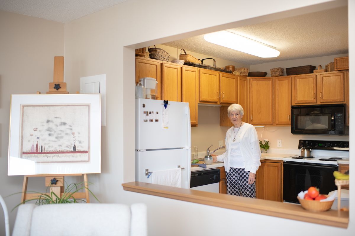 A woman standing in a kitchen of an apartment, with wooden cabinets and a refrigerator.