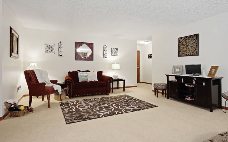A cozy living room with a burgundy sofa, patterned rug, and wall decorations.
