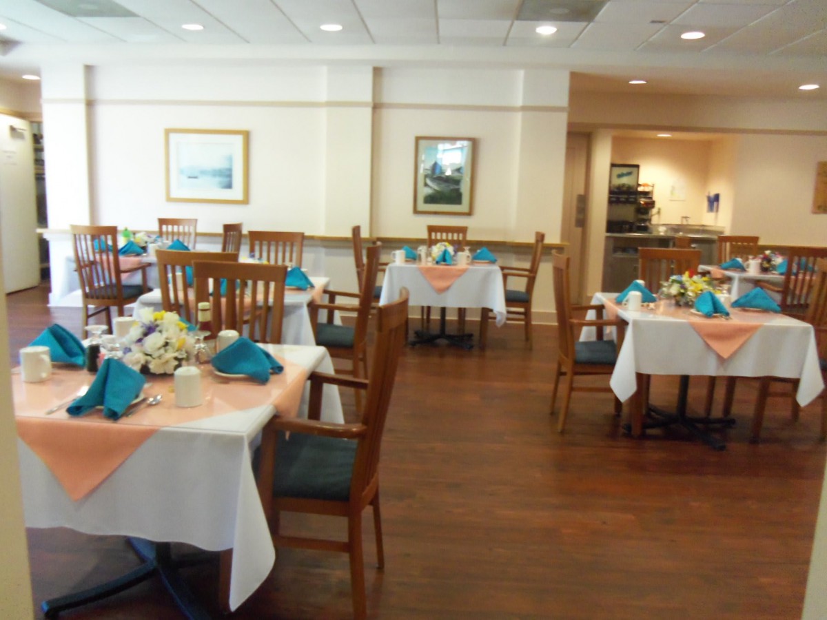 A neatly arranged dining area with tables set for service, featuring wooden chairs and a polished floor.