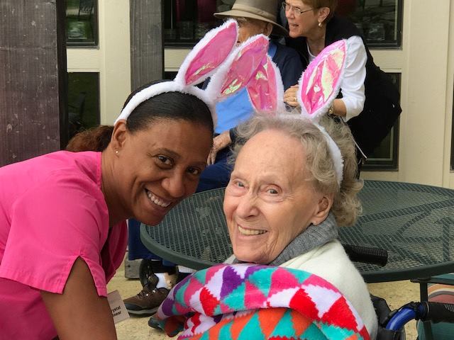 Two individuals wearing bunny ears are smiling outdoors, one wrapped in a colorful blanket.