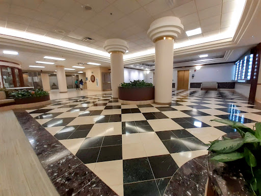 A spacious lobby featuring a checkered floor pattern with decorative columns and greenery.