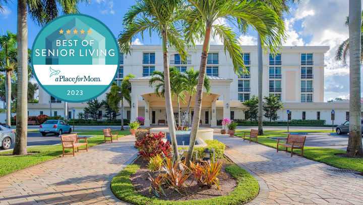 An elegant retirement community building surrounded by lush landscaping and palm trees, with an award emblem displayed.