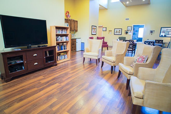 A cozy living room with hardwood floors, a television, bookshelf, and comfortable seating.