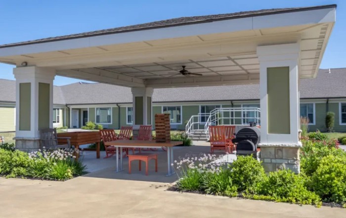 A covered outdoor patio with seating and a garden area under a sunny sky.