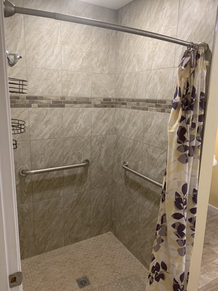 A tiled shower with a floral shower curtain and grab bars for accessibility.